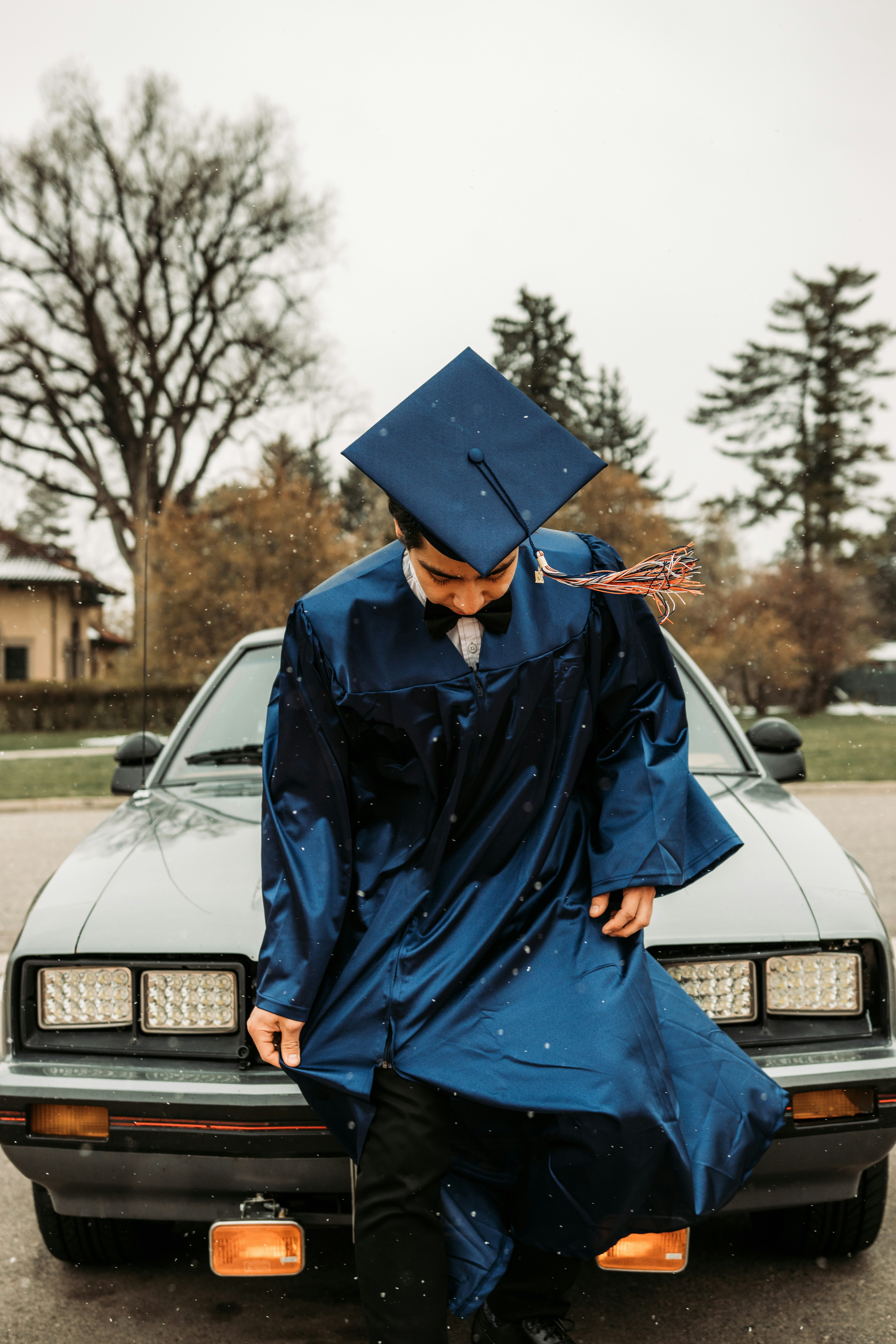 woman in blue academic dress standing beside white car